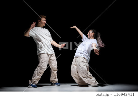 Freestyle. Imagination. Young talented man and woman in light clothes dancing hip-hop against black studio background Freestyle. Imagination. Young talented man and woman in light clothes dancing hip-hop against black studio background 116942411