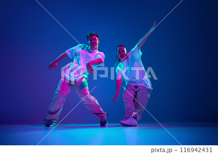 Flexible and energetic young people, man and woman dancing hip-hop, performing with passion against purple studio background in neon light Flexible and energetic young people, man and woman dancing hip-hop, performing with passion against purple studio background in neon light 116942431