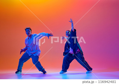 Modern dance school. Young people, man and woman in casual clothes dancing energetically hip-hop against gradient studio background in neon light 116942481
