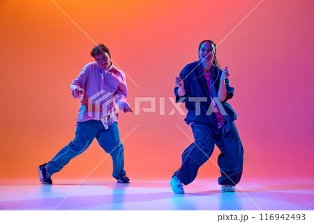 Energy of modern dance styles. Young people, passionate man and woman dancing hip-hop against gradient studio background in neon light Energy of modern dance styles. Young people, passionate man and woman dancing hip-hop against gradient studio background in neon light 116942493