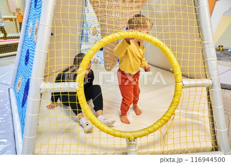 Two children on an indoor playground, unrecognizable children sitting in a maze. A modern colorful mesh playhouse for children in the mall. With space to copy. High quality photo 116944500
