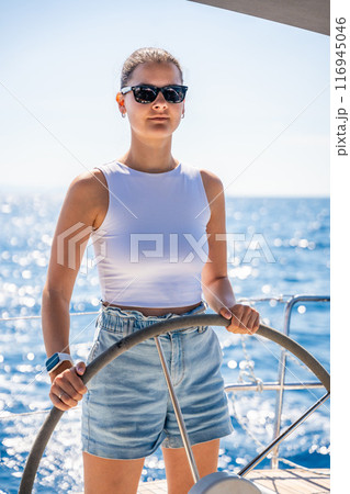 Young woman female captain stands at the helm and controls a sailboat during a journey by sea 116945046