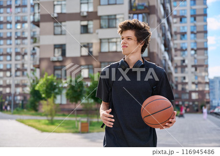 Young male with backpack basketball ball walking outdoors, modern city Young male with backpack basketball ball walking outdoors, modern city 116945486