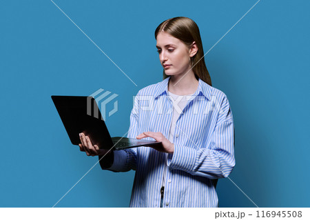 Smiling teenage girl with laptop on blue studio background 116945508