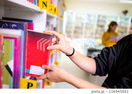 Girl taking a book from shelves in the light school library Girl taking a book from shelves in the light school library 116945681