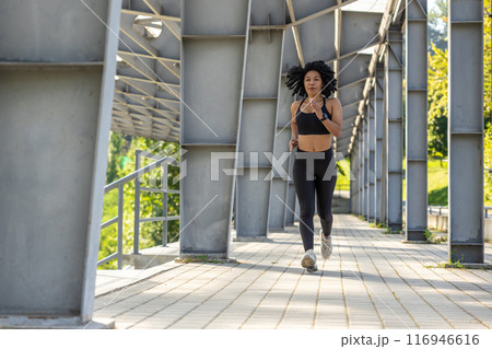 Curly-haired woman in black sportswear running and looking focused 116946616