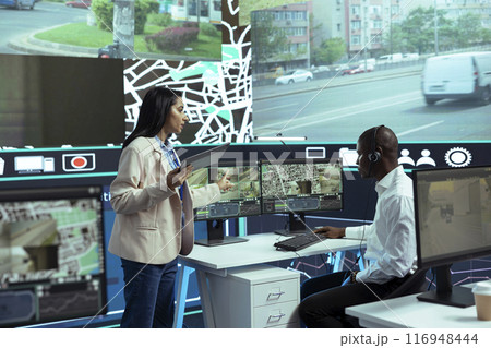 Indian woman coordinates new express shipment program in control center, instructing her team of operators to guide truck drivers through city traffic. Employees offer support via satellite map. 116948444