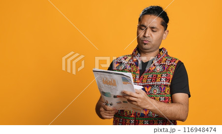 Man browsing though financial audit report files, slapping them in anger, disappointed by results, studio background. Upset indian worker frowning, annoyed by paperwork, camera A 116948474