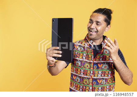 Joyous man having positive mood using tablet to take selfies from all angles. Radiant person taking photos using device selfie camera, feeling stoked, isolated over studio backdrop 116948557