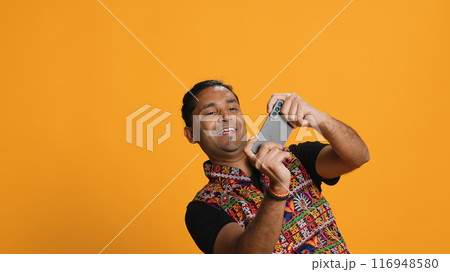 Cheerful Indian person in traditional clothing entertained by videogames on smartphone. Joyous player enjoying game on phone, having fun online, studio backdrop, camera A Cheerful Indian person in traditional clothing entertained by videogames on smartphone. Joyous player enjoying game on phone, having fun online, studio backdrop, camera A 116948580