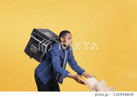 Reckless african american courier spilling a lot of pizza in studio, dropping massive pile of boxes and making a mess. Deliveryman being clumsy and causing an accident, wasting food. Reckless african american courier spilling a lot of pizza in studio, dropping massive pile of boxes and making a mess. Deliveryman being clumsy and causing an accident, wasting food. 116948609