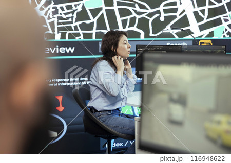 Call center operator puts headphones on to handle order delays complains from customers, working to ensure faster delivery time via satellite map and CCTV system. Cargo tracing. 116948622