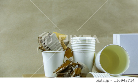 White paper coffee cup, used paper, and cardboard box on a brown surface, awaiting recycling. White paper coffee cup, used paper, and cardboard box on a brown surface, awaiting recycling. 116948714