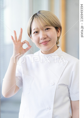 ケーシー白衣を着る金髪ショートヘアの若い女性整体師（髪色自由、自分らしく働く、職場環境） 116949394