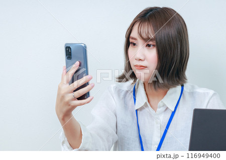 渋い顔でスマホを見ている女性スタッフ 渋い顔でスマホを見ている女性スタッフ 116949400