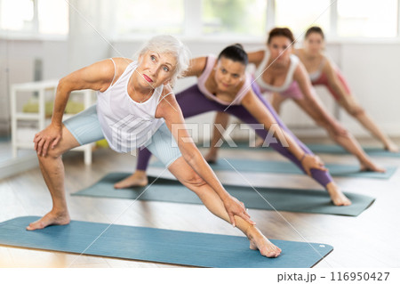 Women practicing in yoga class, focusing on flexibility and relaxation in calm studio setting 116950427