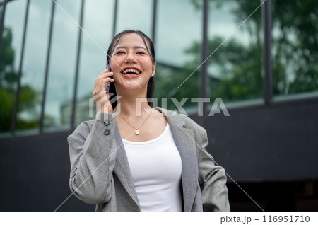 A confident Asian businesswoman in a suit is talking on the phone while walking in the city. 116951710