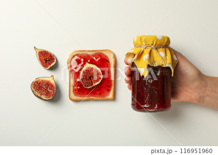 Figs, jar of jam in hand and piece of bread on white background, top view 116951960