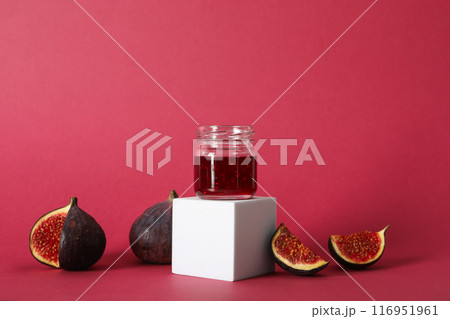 Figs and jar of jam on white block on pink background 116951961