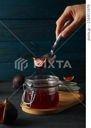 Figs, jar of jam and spoon in hand on blue wooden background 116951976