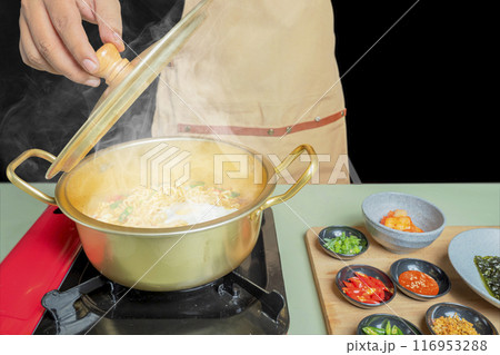 A person is cooking instant noodles in a pot with a lid on top 116953288