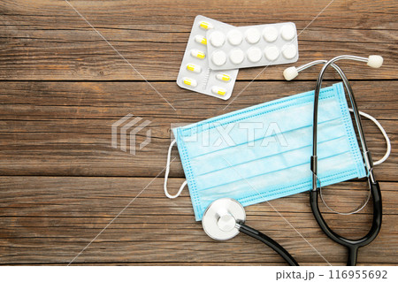 Composition with medical stethoscope, disposable face masks, pills on grey wooden background. Composition with medical stethoscope, disposable face masks, pills on grey wooden background. 116955692
