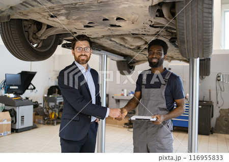 Businessman shaking hands with mechanic under car lift in garage Businessman shaking hands with mechanic under car lift in garage 116955833