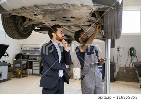 Mechanic explaining car inspection to business professional in auto repair shop 116955858