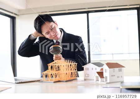 虫眼鏡で建築模型を覗くスーツ姿の悩む男性 116957729