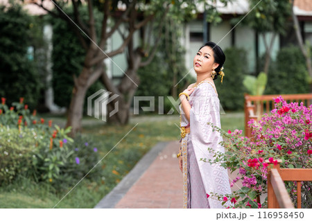 A woman in a traditional Thai costumes is standing on the wooden bridge while being taken a portrait photo shooting. A woman in a traditional Thai costumes is standing on the wooden bridge while being taken a portrait photo shooting. 116958450