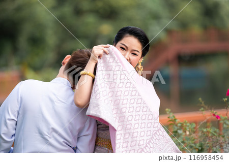 A woman in a traditional Thai costumes is standing on the wooden bridge while being taken a portrait photo shooting. A woman in a traditional Thai costumes is standing on the wooden bridge while being taken a portrait photo shooting. 116958454