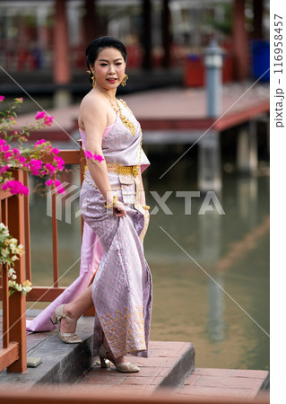 A woman in a traditional Thai costumes is standing on the wooden bridge while being taken a portrait photo shooting. A woman in a traditional Thai costumes is standing on the wooden bridge while being taken a portrait photo shooting. 116958457