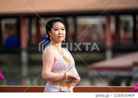 A woman in a traditional Thai costumes is standing on the wooden bridge while being taken a portrait photo shooting. A woman in a traditional Thai costumes is standing on the wooden bridge while being taken a portrait photo shooting. 116958464