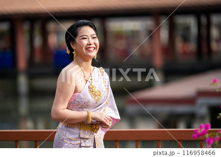 A woman in a traditional Thai costumes is standing on the wooden bridge while being taken a portrait photo shooting. 116958466