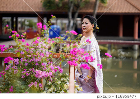 A woman in a traditional Thai costumes is standing on the wooden bridge while being taken a portrait photo shooting. 116958477