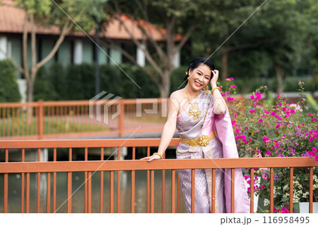 A woman in a traditional Thai costumes is standing on the wooden bridge while being taken a portrait photo shooting. 116958495