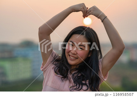 Asian Chinese Thai woman plays with the sun shape on rooftop in twilight time. 116958507