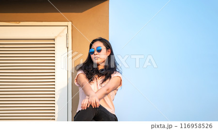 Sun Glasses Asian woman is sitting on the rooftop barricade cement (not dangerous because the opposite site is rooftop floor as well) in front of empty sky. 116958526