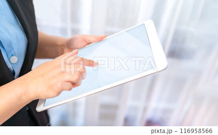 Close up to the White empty screen tablet which hold by Asina women in black suit in front of transparent curtain Close up to the White empty screen tablet which hold by Asina women in black suit in front of transparent curtain 116958566