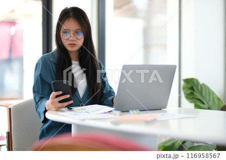 A woman is sitting at a table with a laptop and a cell phone A woman is sitting at a table with a laptop and a cell phone 116958567