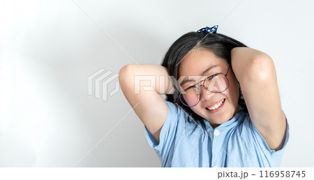 A young asian girl touch her hair smoothly with a big smile on her face. She is wearing a light blue shirt and glasses. 116958745