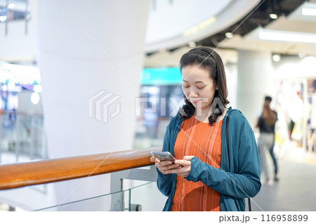 Beautiful Asian Woman holds and plays mobile phone in Department Store atmosphere environment in Bangkok City. Beautiful Asian Woman holds and plays mobile phone in Department Store atmosphere environment in Bangkok City. 116958899
