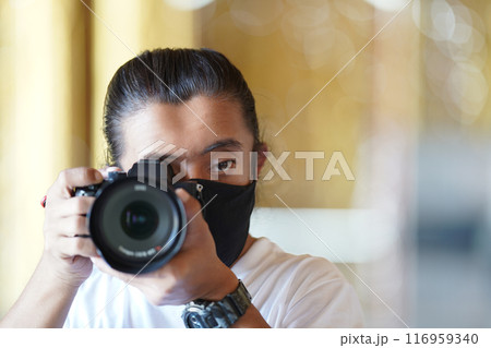 A man wearing black mask is shooting photo through a viewfinder camera with the right eye. 116959340