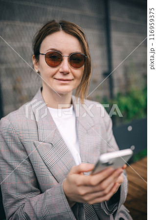 A woman in a plaid blazer smiles while checking her phone on a sunny day A woman in a plaid blazer smiles while checking her phone on a sunny day 116959375
