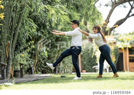Asian Man and woman taking a pre wedding photo with woman grabbing his shoulder and bracing the man in the garden. 116959384
