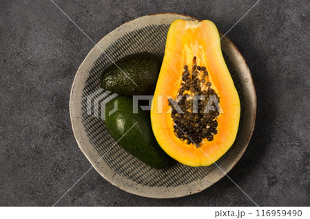 Two avocados and half a papaya on a gray clay plate Two avocados and half a papaya on a gray clay plate 116959490