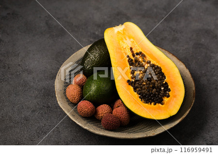 Two avocados, half a papaya and lychee berries on a gray clay plate 116959491