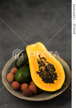 Two avocados, half a papaya and lychee berries on a gray background Two avocados, half a papaya and lychee berries on a gray background 116959492