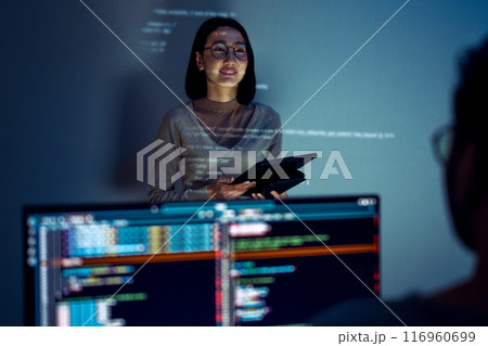 asian woman developers collaborating on a coding project, with one member presentation at code projected on the wall while the other works on multiple computer screens asian woman developers collaborating on a coding project, with one member presentation at code projected on the wall while the other works on multiple computer screens 116960699