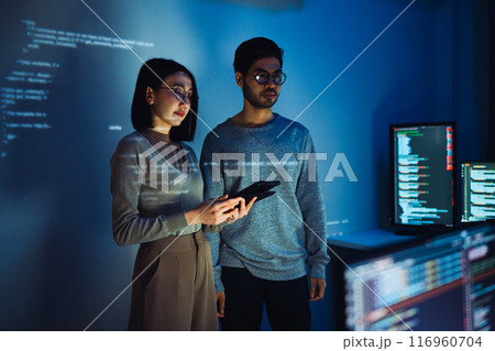 Asian Two software developers engaged in collaborative coding session, with code projected onto the wall and multiple computer screens displaying 116960704